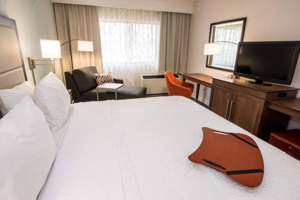 A hotel room with a large bed, a desk with a television, a chair, and a window with curtains.