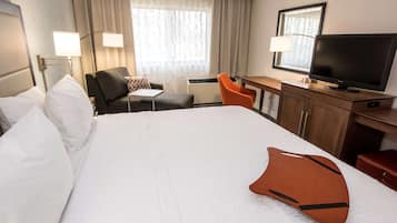 A hotel room with a large bed, a desk with a television, a chair, and a window with curtains.