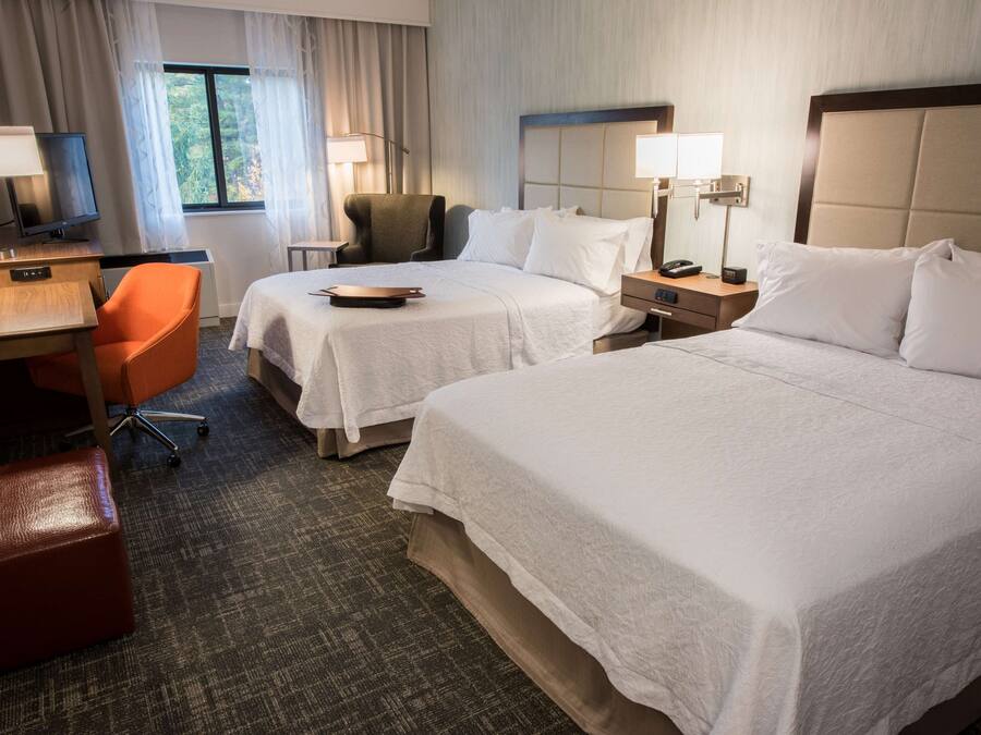 A hotel room with two beds, a desk with a chair, a TV, and a window with curtains.