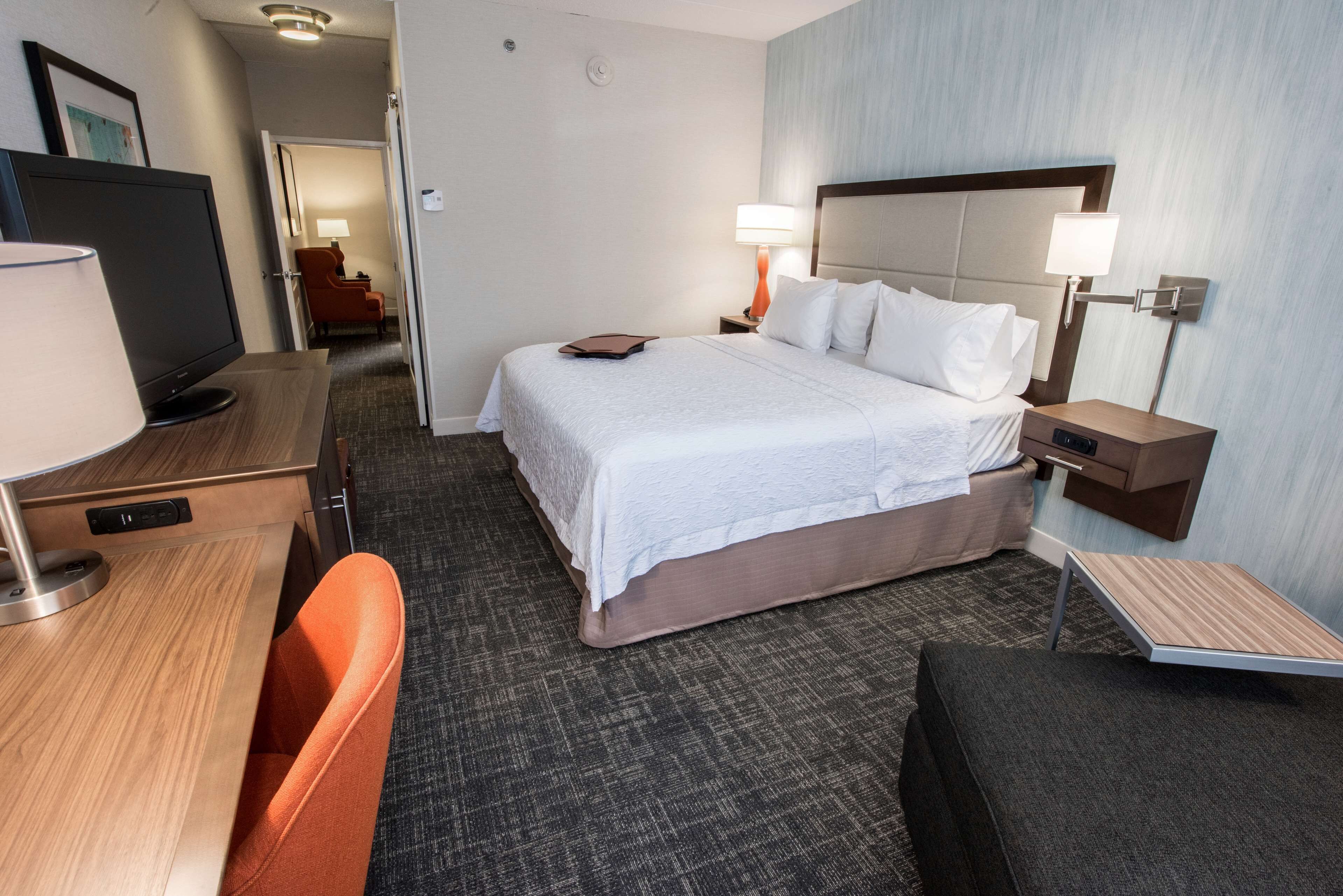 A hotel room with a bed, bedside tables, a desk, a chair, and a TV.