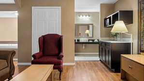 A living room with a red armchair, a wooden coffee table, and a brown sofa. There is a kitchen area with a microwave, a sink, and a cabinet. - Signature Inn Danville (Danville)
