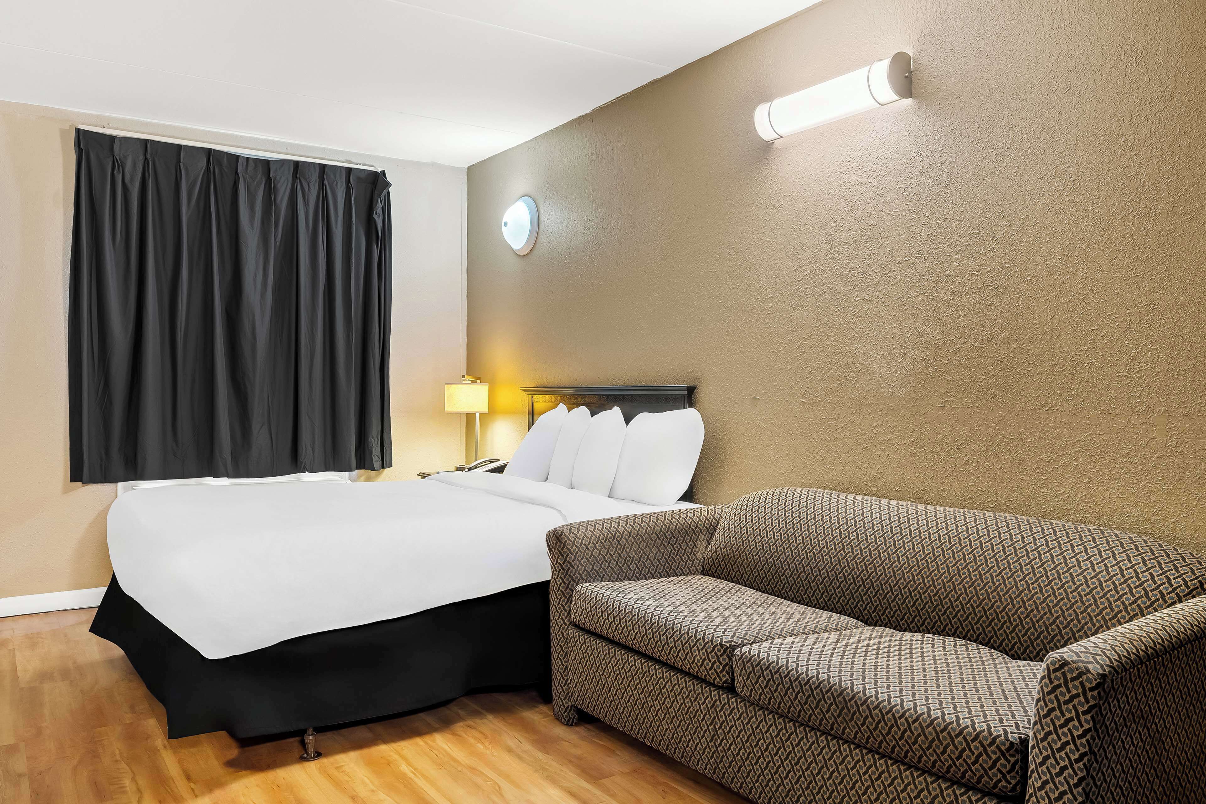 Una habitación de hotel con cama, sofá, lámpara y un reloj de pared.