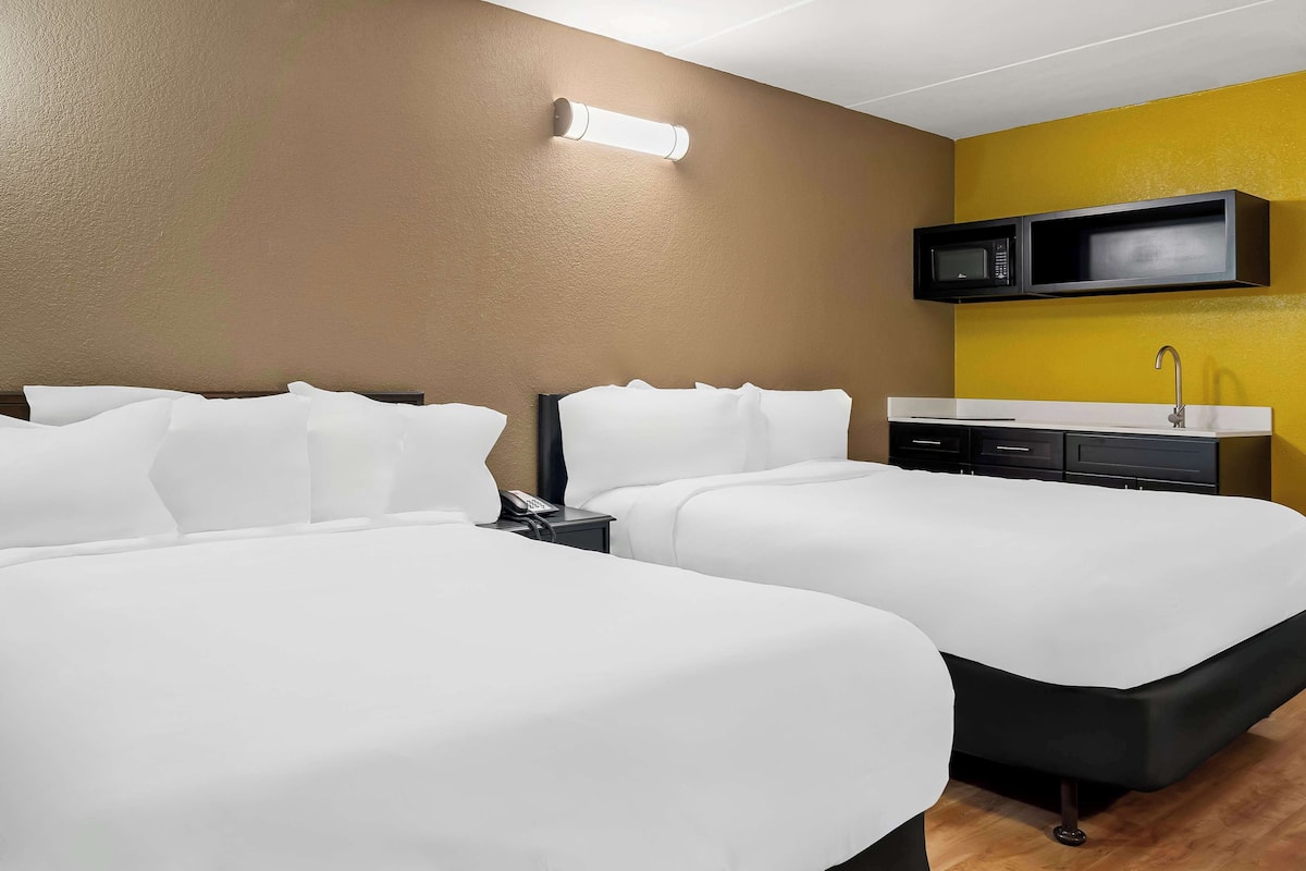 A hotel room with two beds, a microwave, a sink, and a telephone on a nightstand.