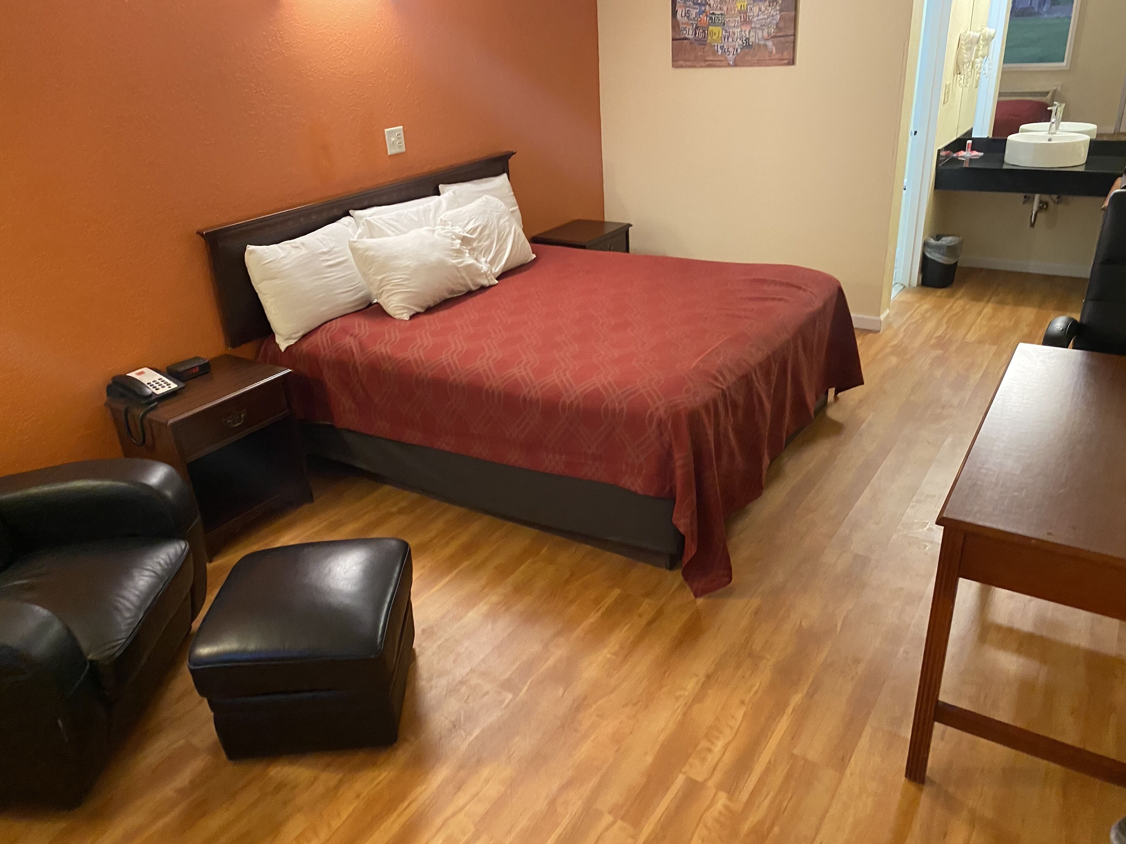 A bedroom with a bed, a nightstand, a desk, a chair, and a small table.