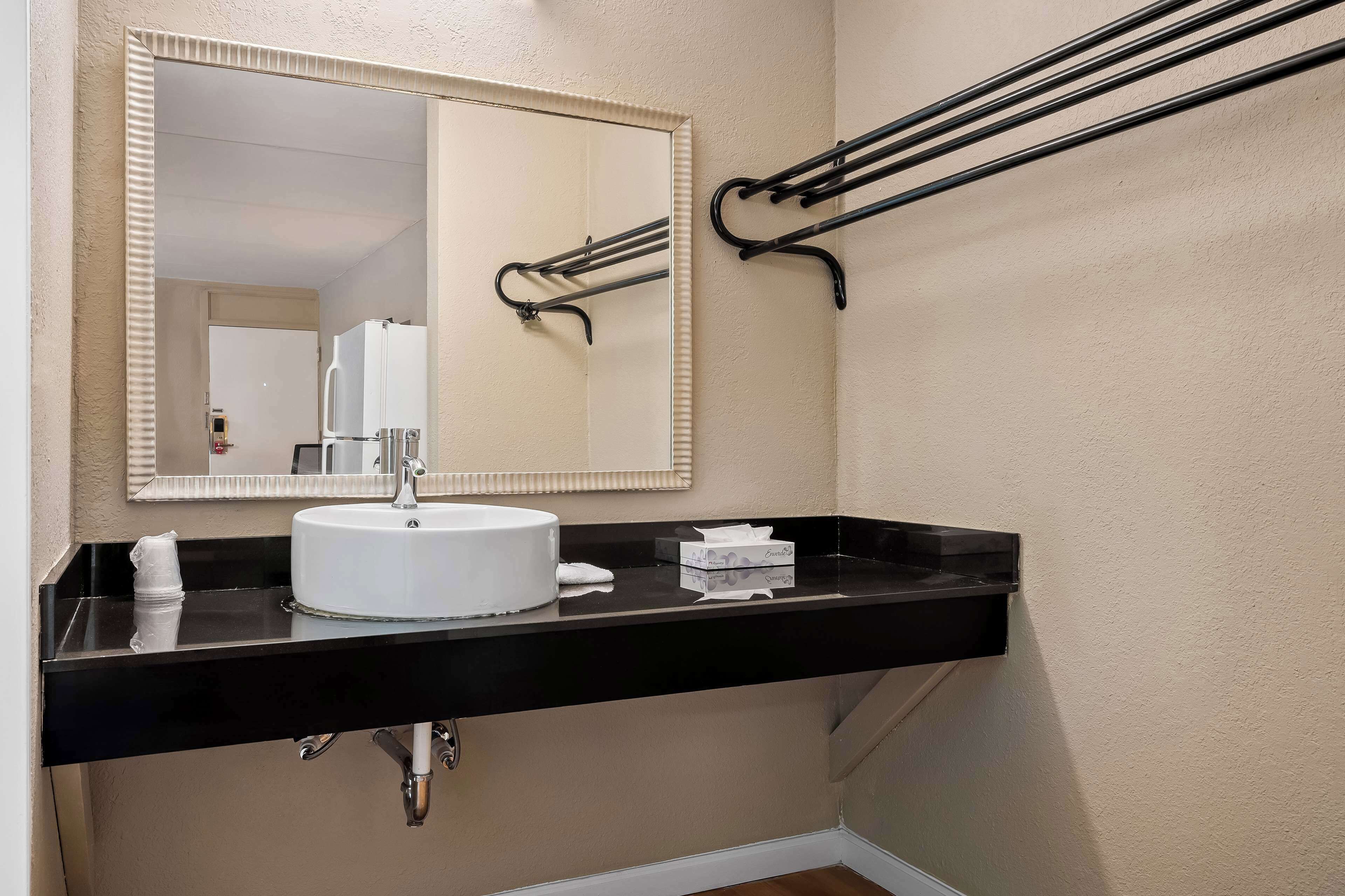 A bathroom with a white sink, black countertop, and a mirror with a beige frame.