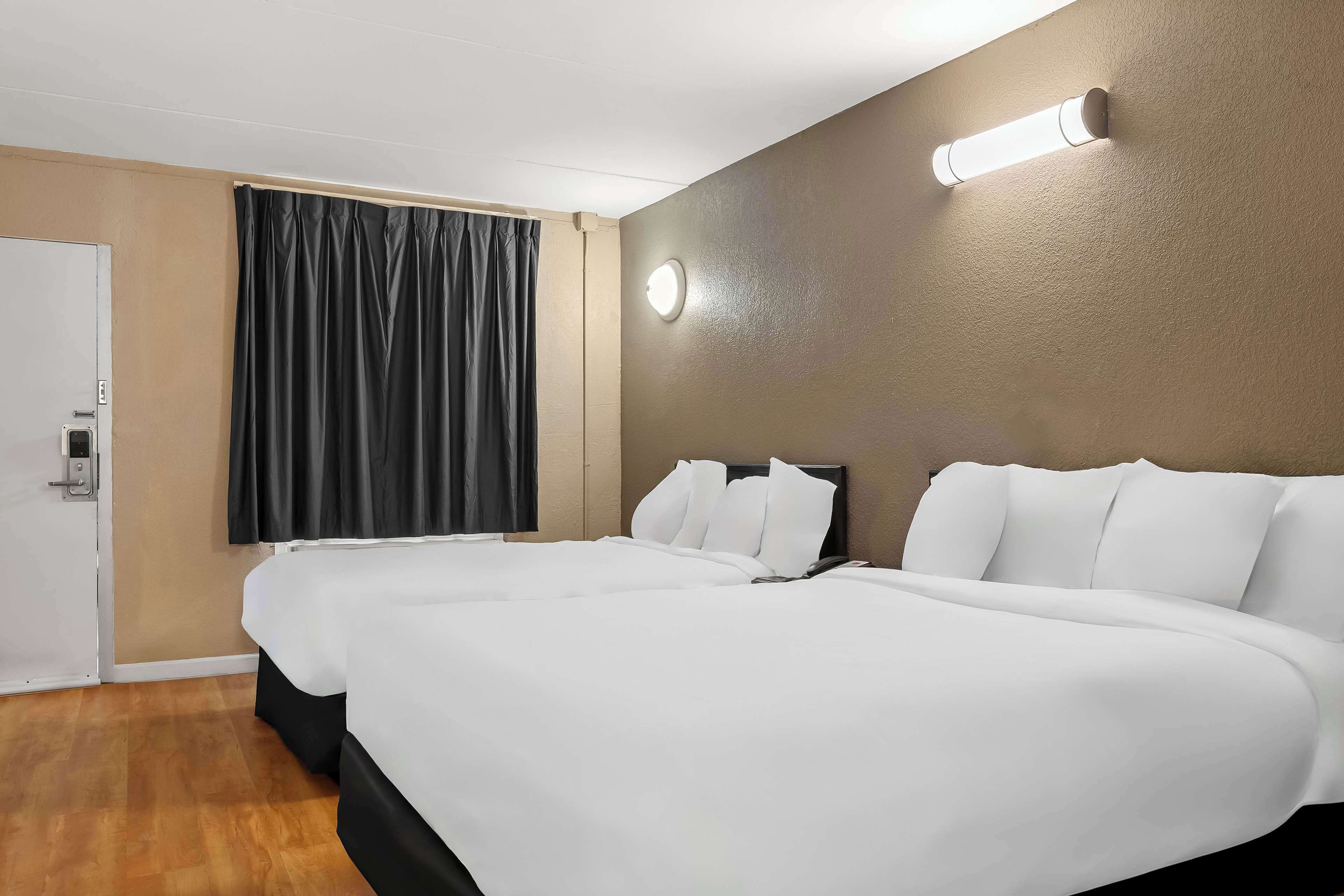 Habitación de hotel con dos camas, un ventanal con cortinas, una lámpara de pared y una puerta con manija.