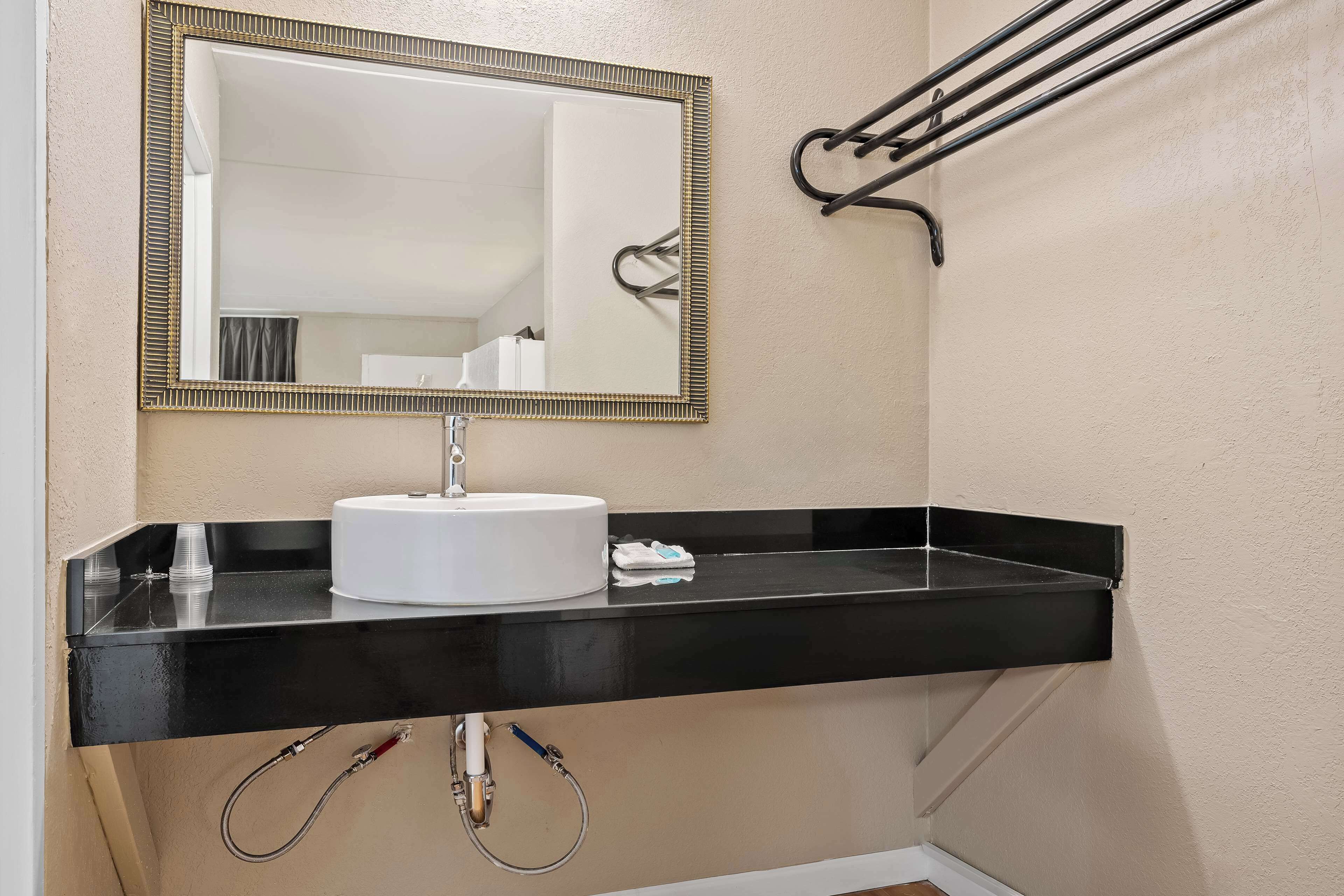 A bathroom with a black countertop, white sink, and a mirror with a gold frame.