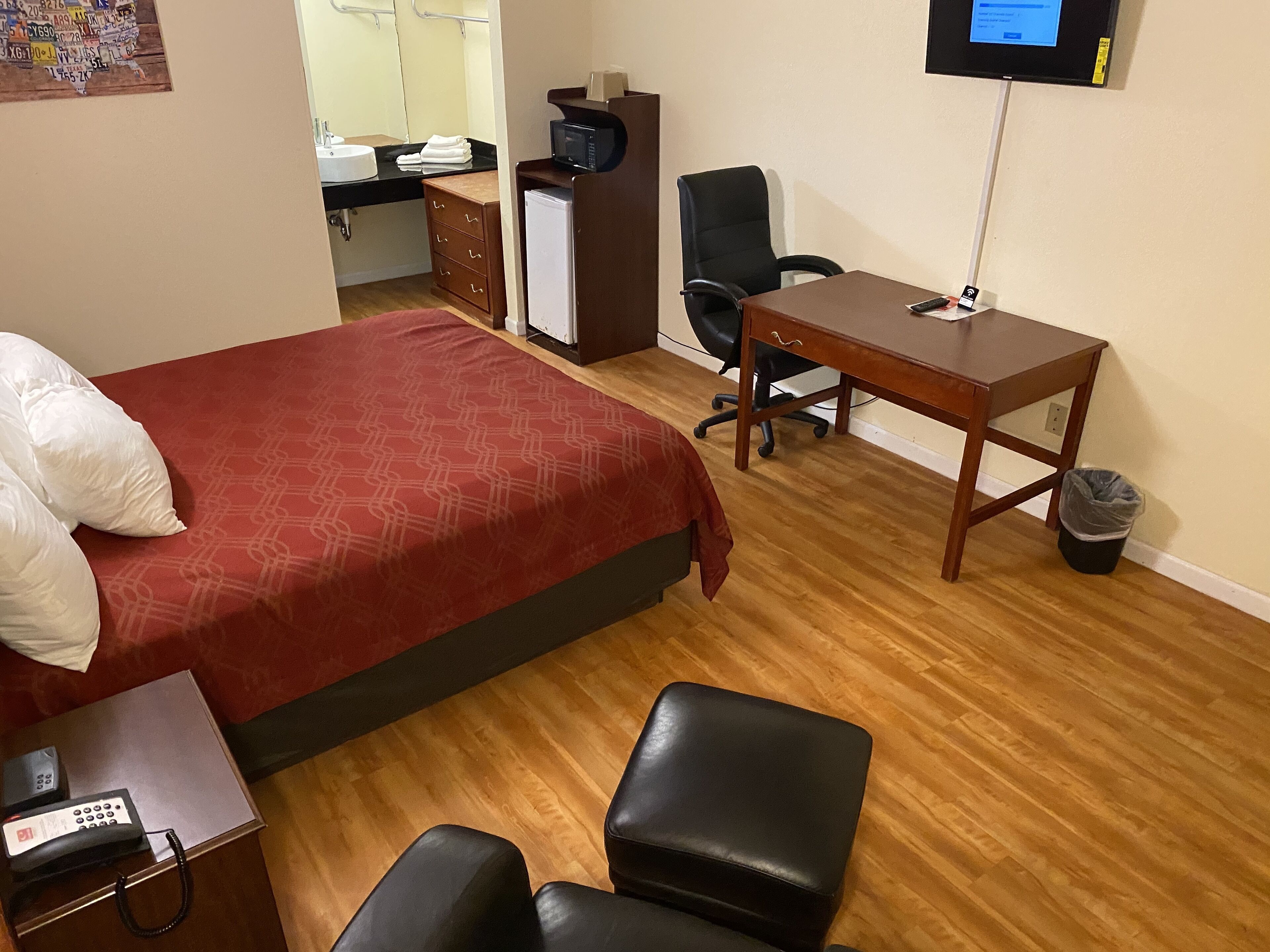 A hotel room with a bed, a desk, a chair, a trash bin, a TV, and a telephone.