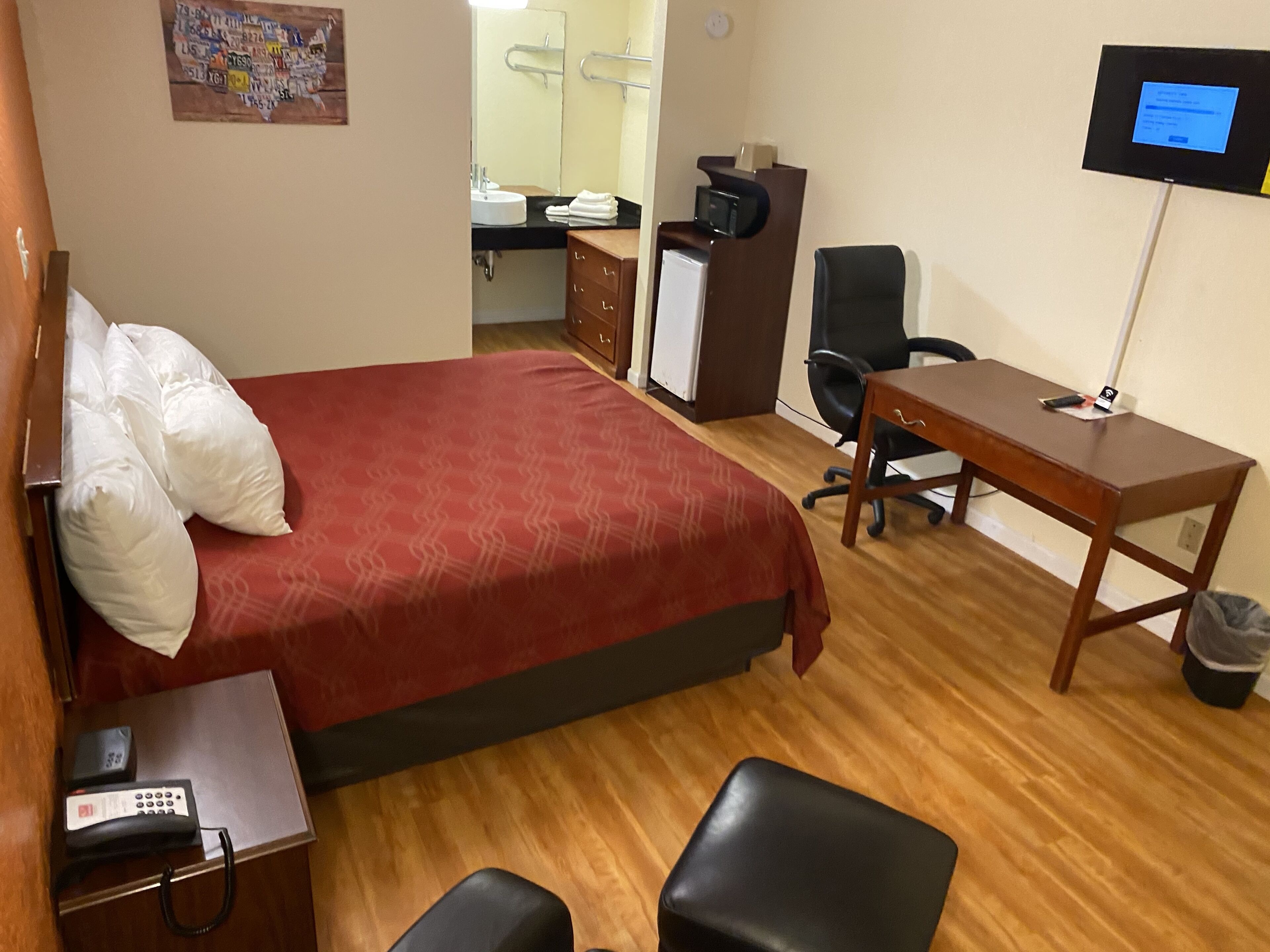A hotel room with a bed, a desk, a chair, a TV, a desk lamp, a telephone, and a trash bin.