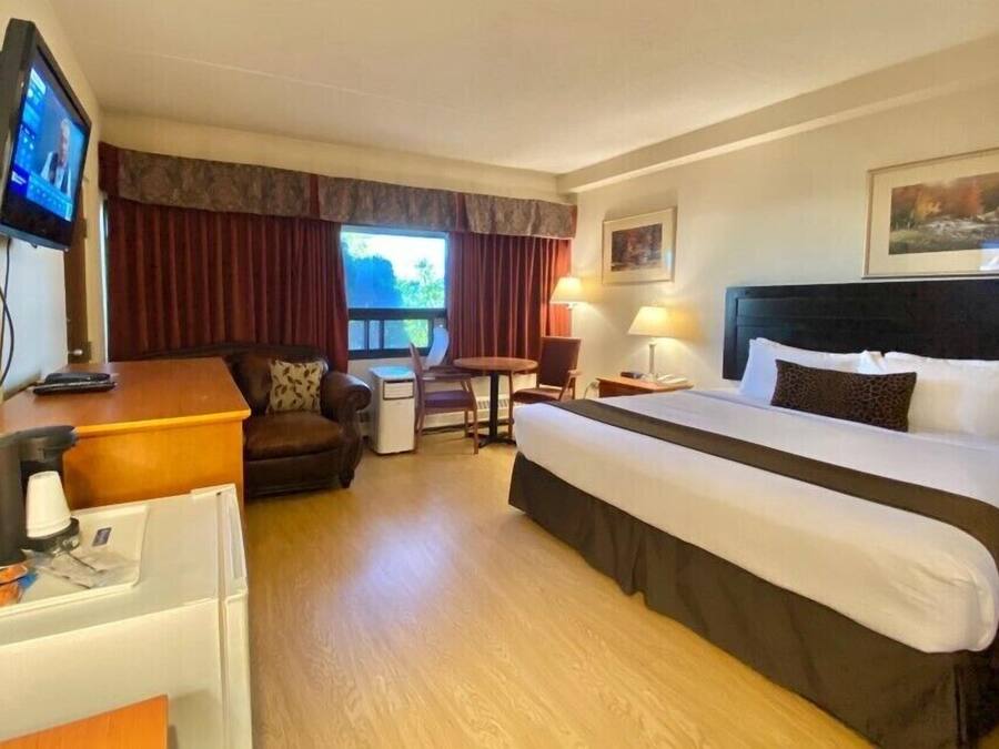 Una habitación de hotel con una cama grande, un escritorio con computadora, una silla, una mesita y una ventana con cortinas.