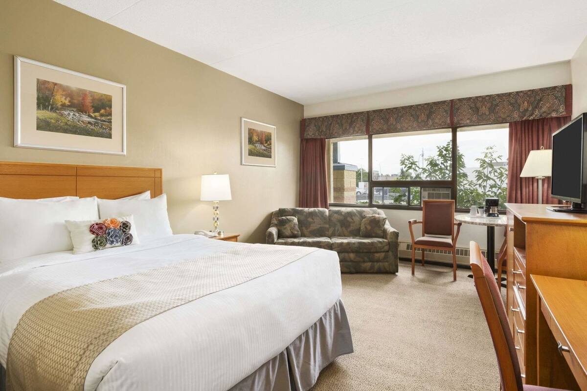 Een hotelkamer met een groot bed, een bank, een bureau met een televisie en een raam met uitzicht.