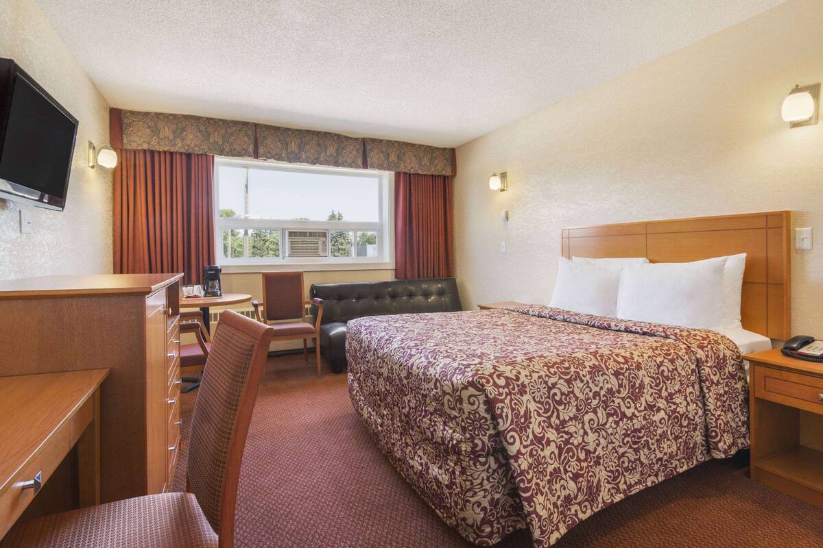 Een hotelkamer met een bed, bureau, stoel, televisie en een raam met gordijnen.
