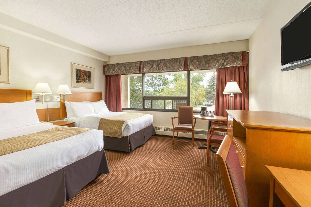 Een hotelkamer met twee bedden, een bureau, een stoel, een televisie en een raam met gordijnen.