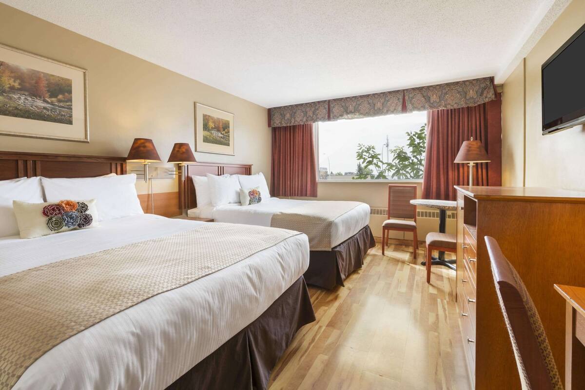Een hotelkamer met twee bedden, een bureau, een stoel, een televisie en een raam met gordijnen.