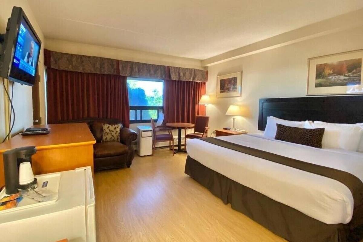 Een hotelkamer met een bed, een bureau, een stoel, een televisie en een raam met gordijnen.