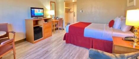 A hotel room with a bed, a desk with a computer, a chair, and a television.