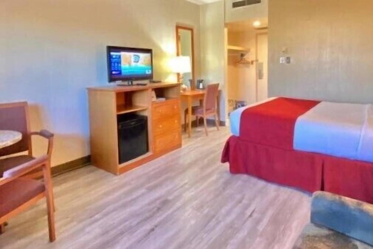 Een hotelkamer met een bed, bureau, stoel, televisie en een kleine kitchenette.