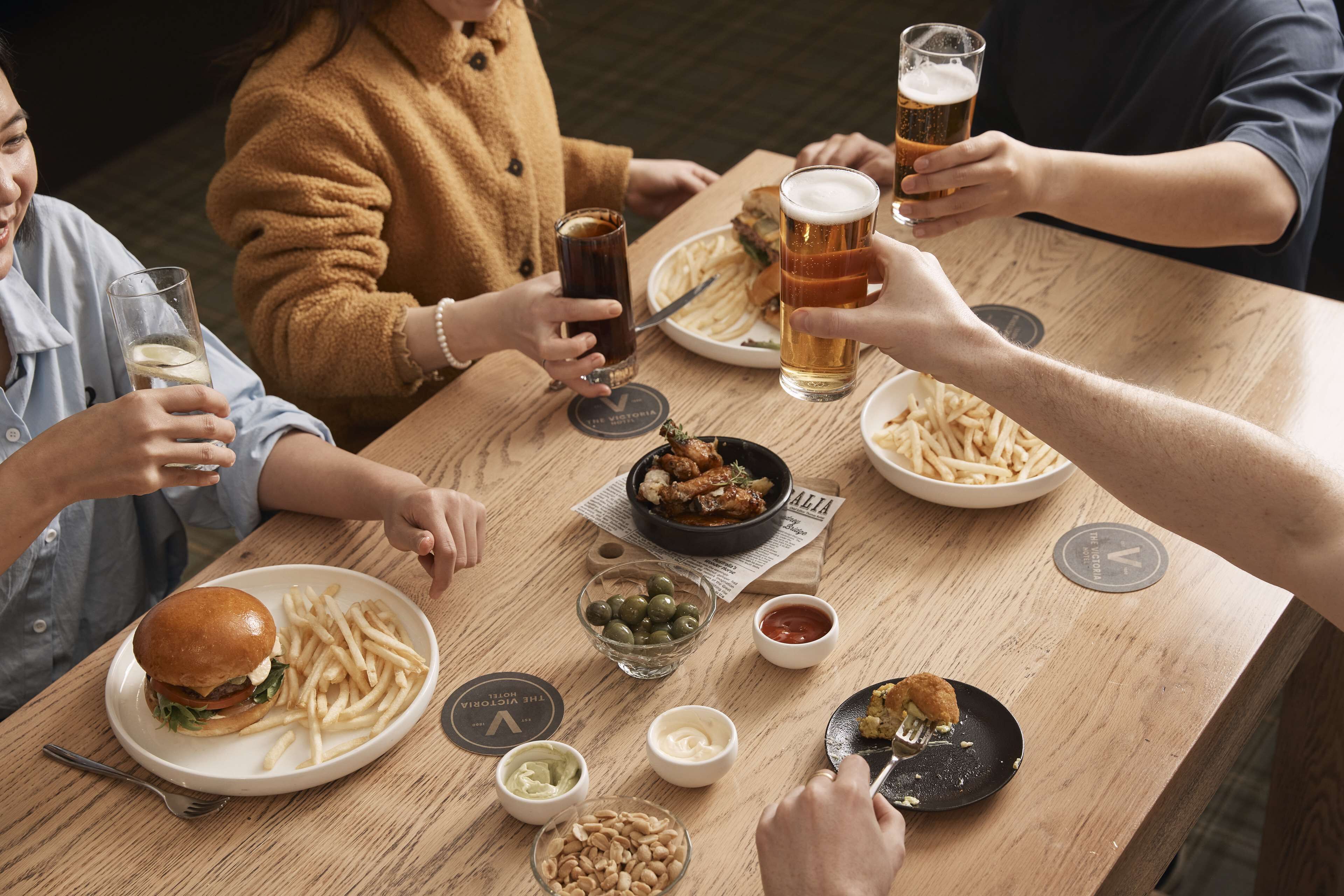 A group of people sitting around a wooden table, enjoying a meal with burgers, fries, and various condiments.