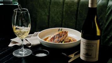 A bottle of wine, a glass, and a bowl of food on a table.