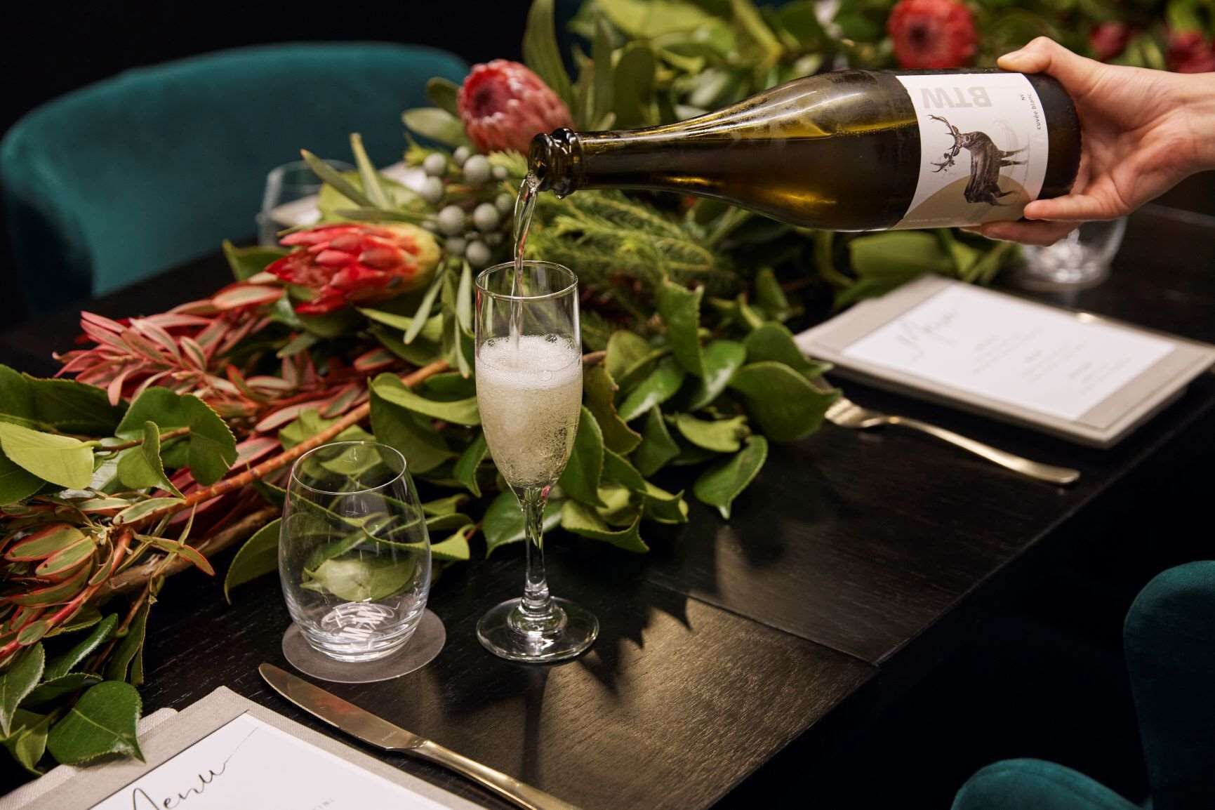 A bottle of wine being poured into a glass on a table with a menu and a knife.