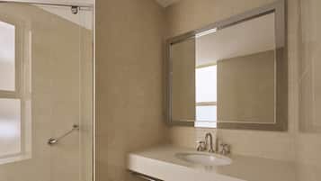 A bathroom with a glass shower door, a sink with a mirror, and beige tiles.