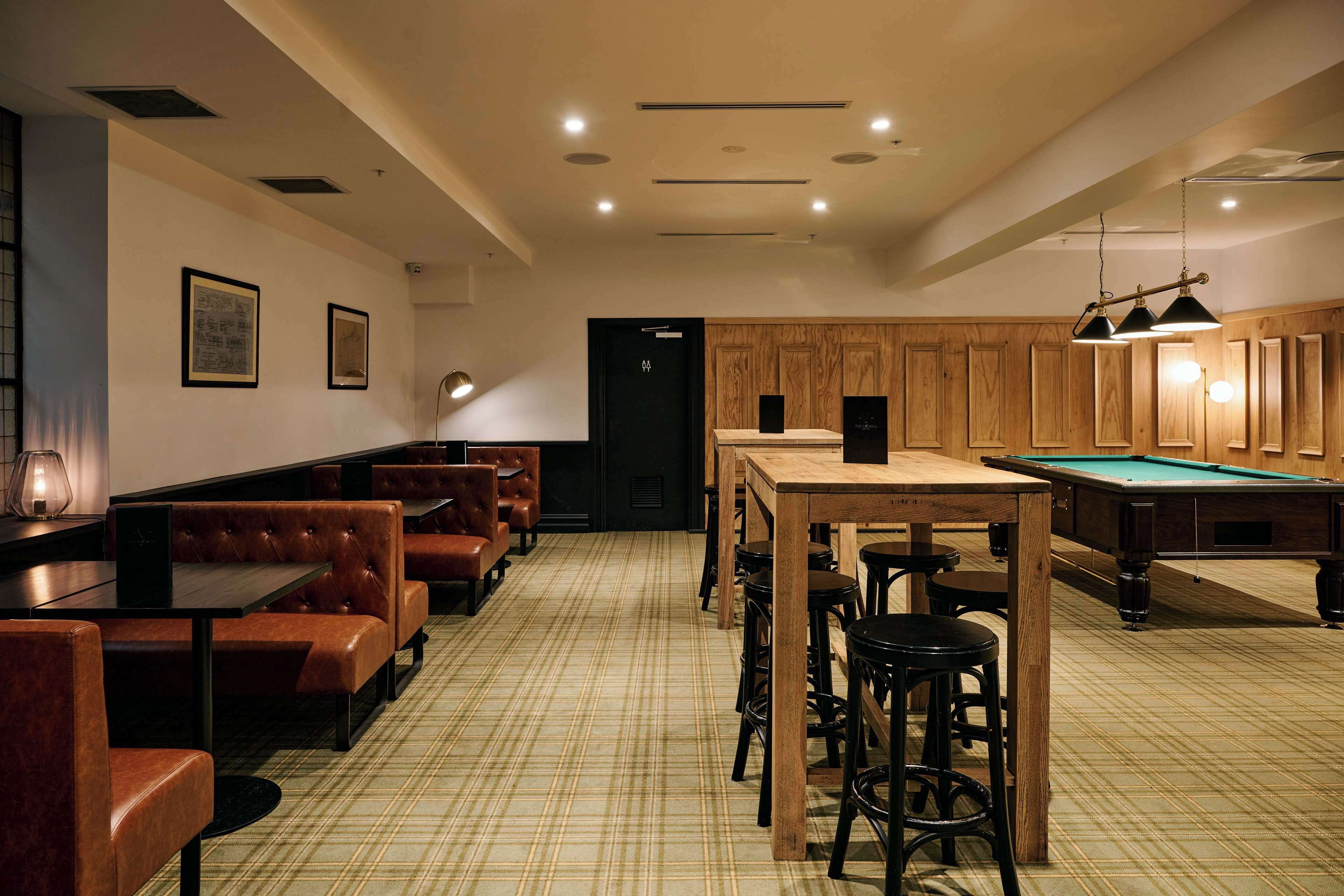 A billiards room with wooden cabinets, a pool table, and multiple seating areas with leather booths and stools.