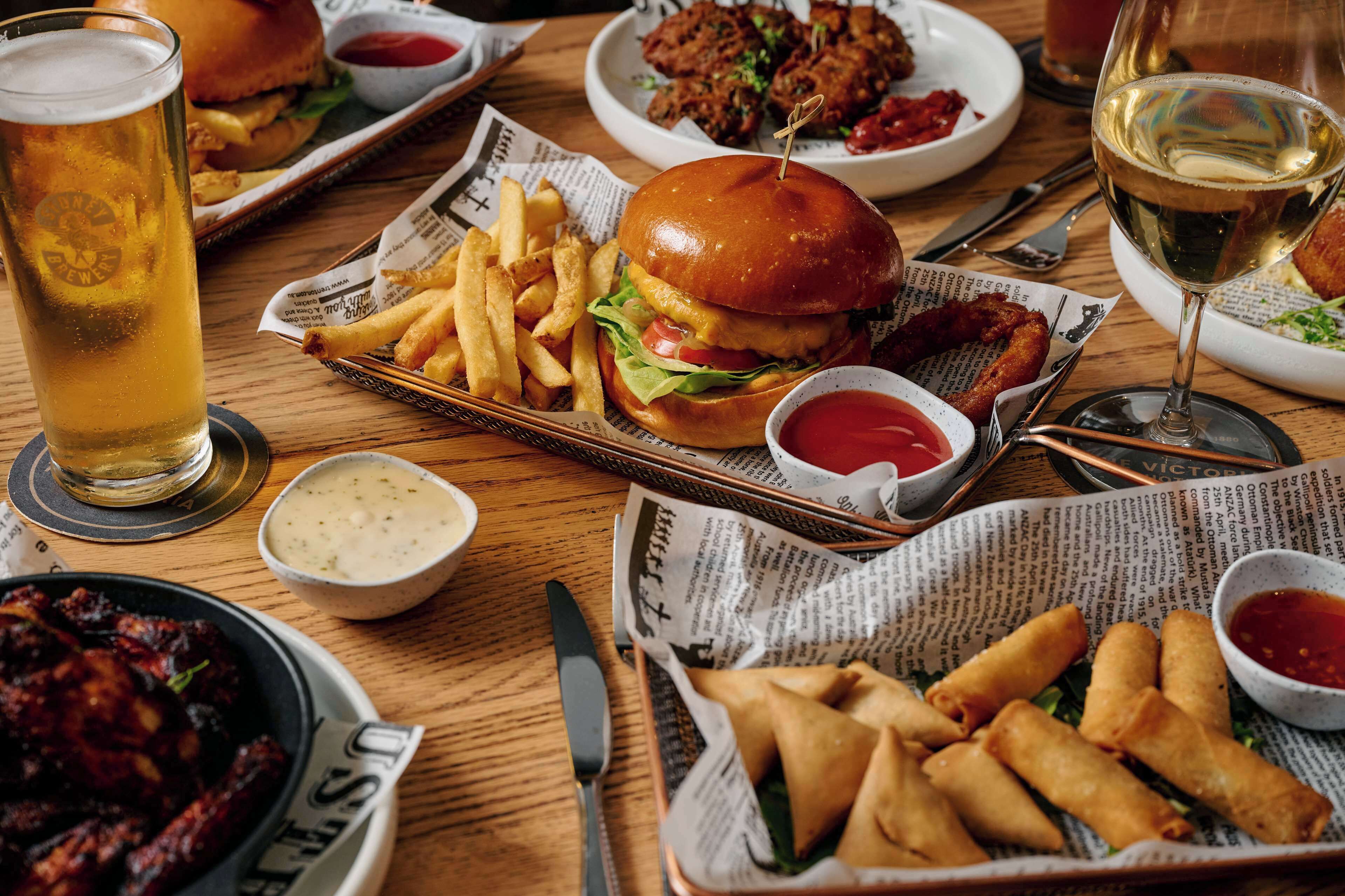 A meal with a burger, fries, and a glass of beer on a wooden table.
