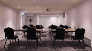 Un salón de conferencias con una larga mesa, sillas negras y una pantalla de proyector.