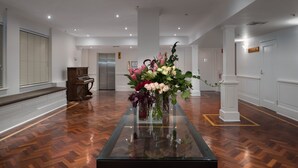 A spacious lobby with a polished wooden floor, a glass-top table with a floral arrangement, and a grand piano in the background. - The Victoria Hotel Melbourne (Melbourne)