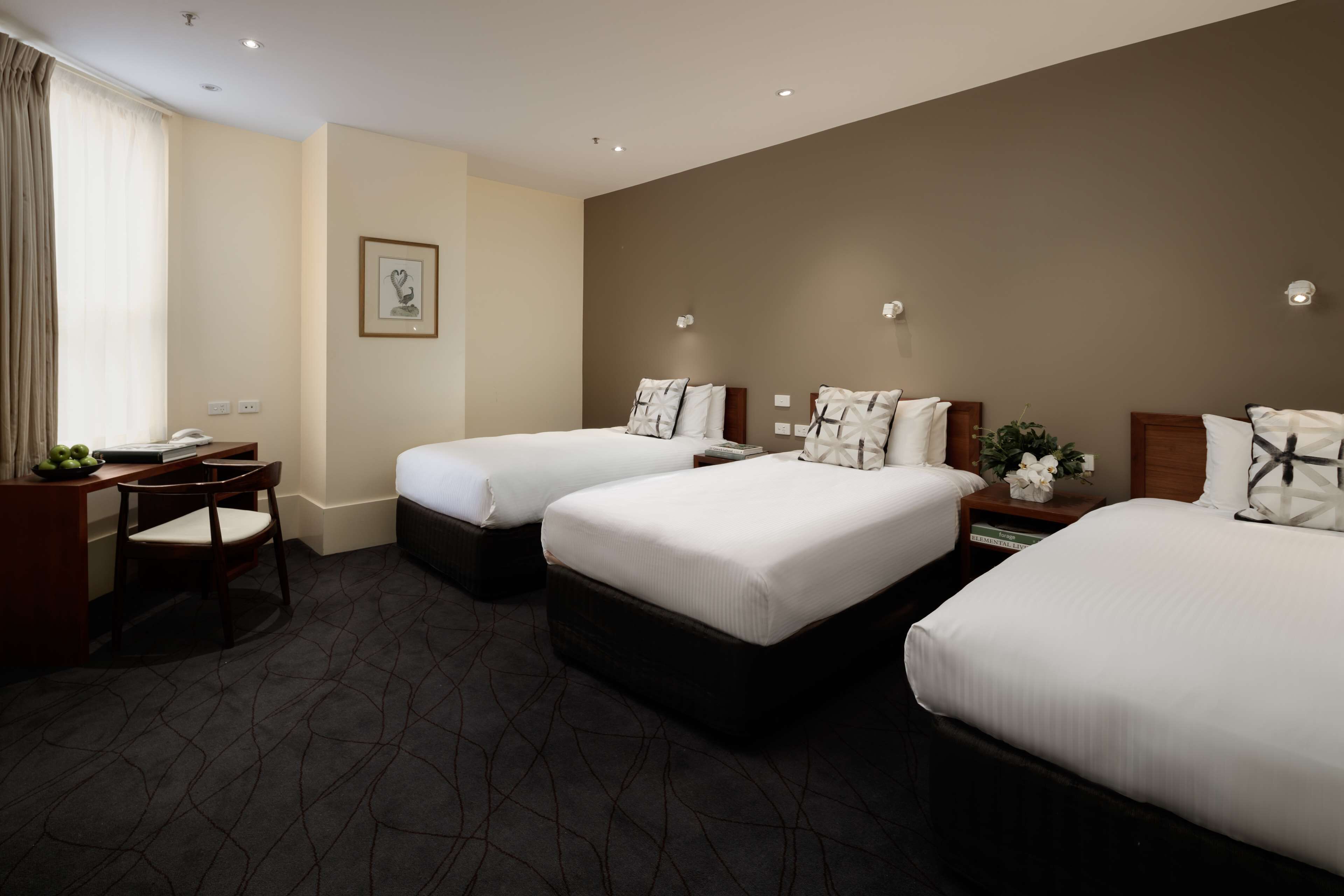 Une chambre d’hôtel avec deux lits, un bureau avec une chaise, un téléphone et un tableau encadré au mur.