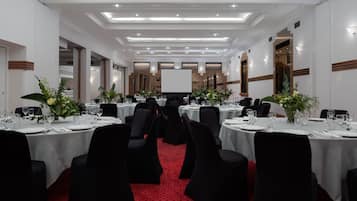 Een feestzaal met ronde tafels, zwarte stoelen en witte tafelkleden.