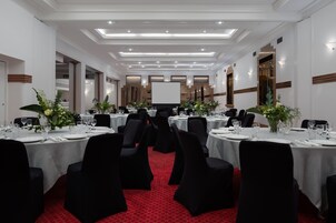 Un salón de banquetes con mesas redondas, sillas negras y manteles blancos.