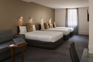 A hotel room with two beds, a sofa, a laptop on a side table, and a TV mounted on the wall.