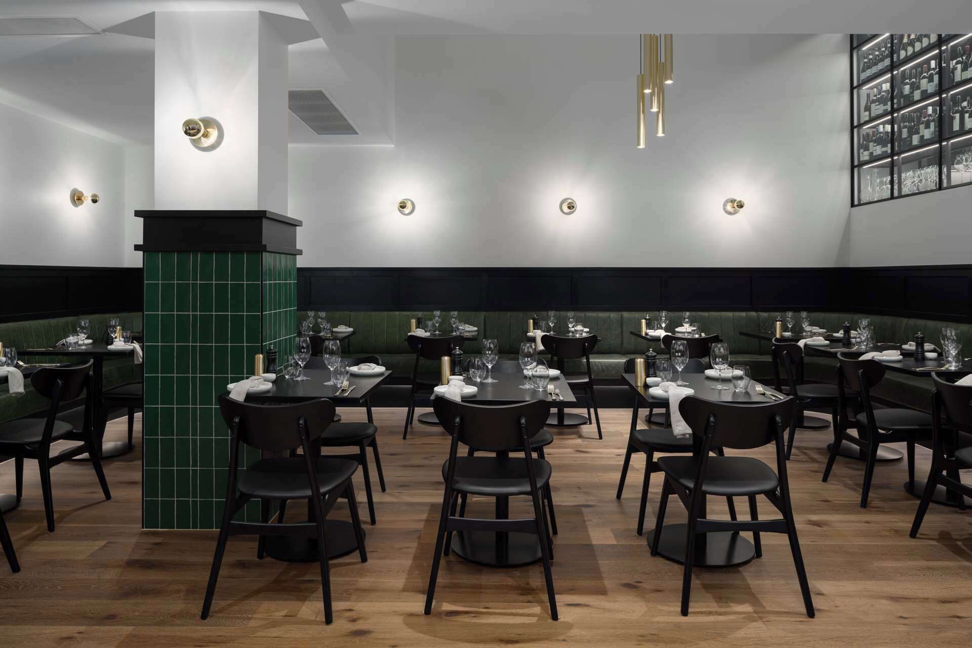 A restaurant with multiple tables and chairs, a green accent wall, and pendant lighting.