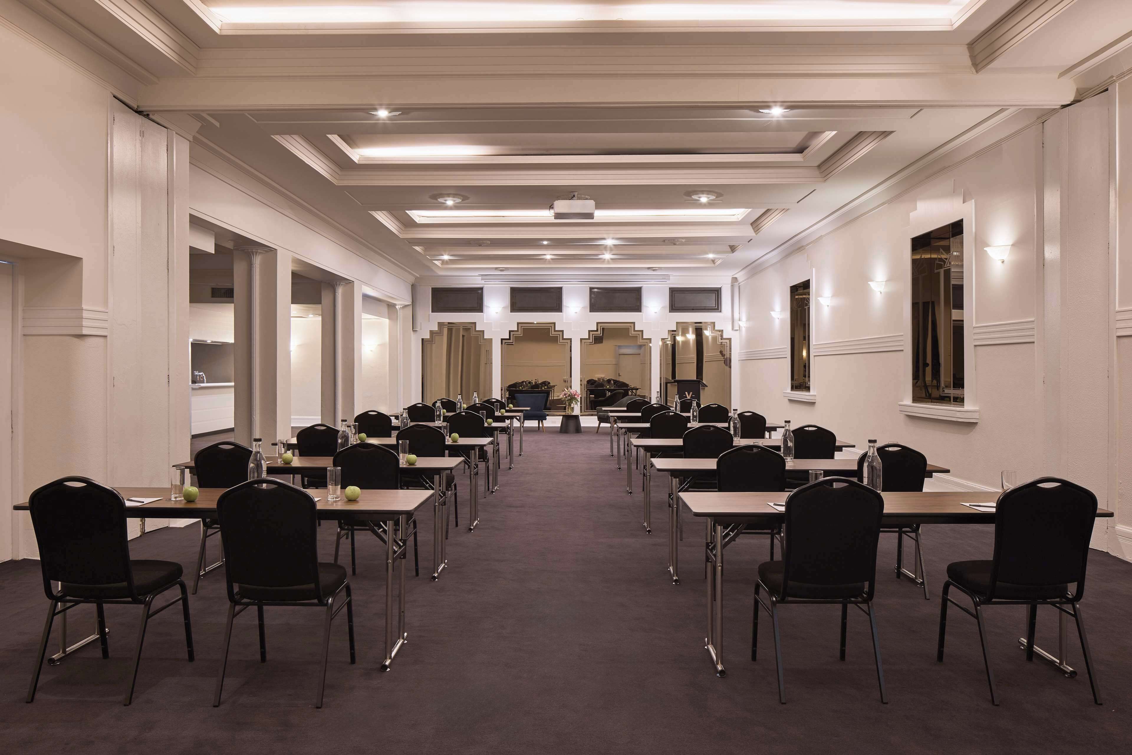 A conference room with multiple tables and chairs, a carpeted floor, and a ceiling with recessed lighting.