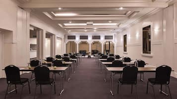 Un salón de conferencias con varias mesas y sillas, piso alfombrado e iluminación empotrada en el techo.