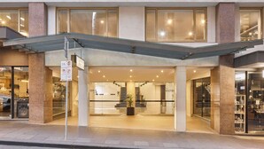 The exterior of The Victoria Hotel with a modern design, featuring large glass windows, a prominent entrance, and a staircase leading to the lobby. - The Victoria Hotel Melbourne (Melbourne)
