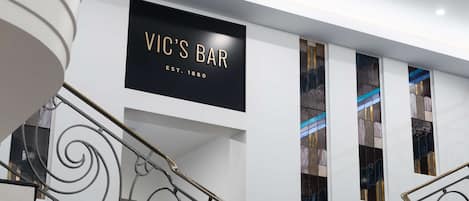 A staircase with ornate metal railings and a sign for VIC'S BAR, established in 1880, on the wall.