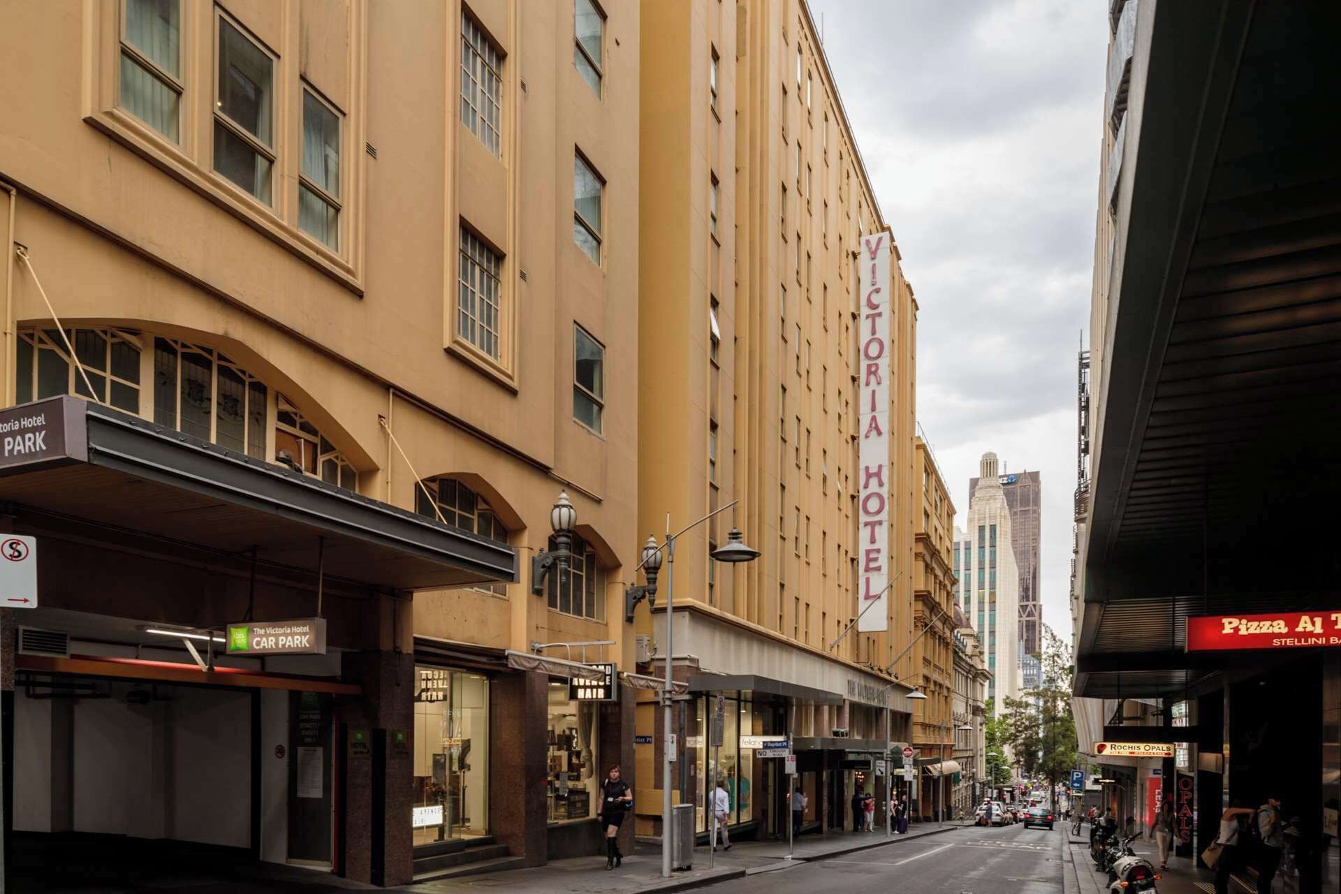 Vista de una calle con el Hotel Victoria, un edificio amarillo con múltiples ventanas y un letrero.