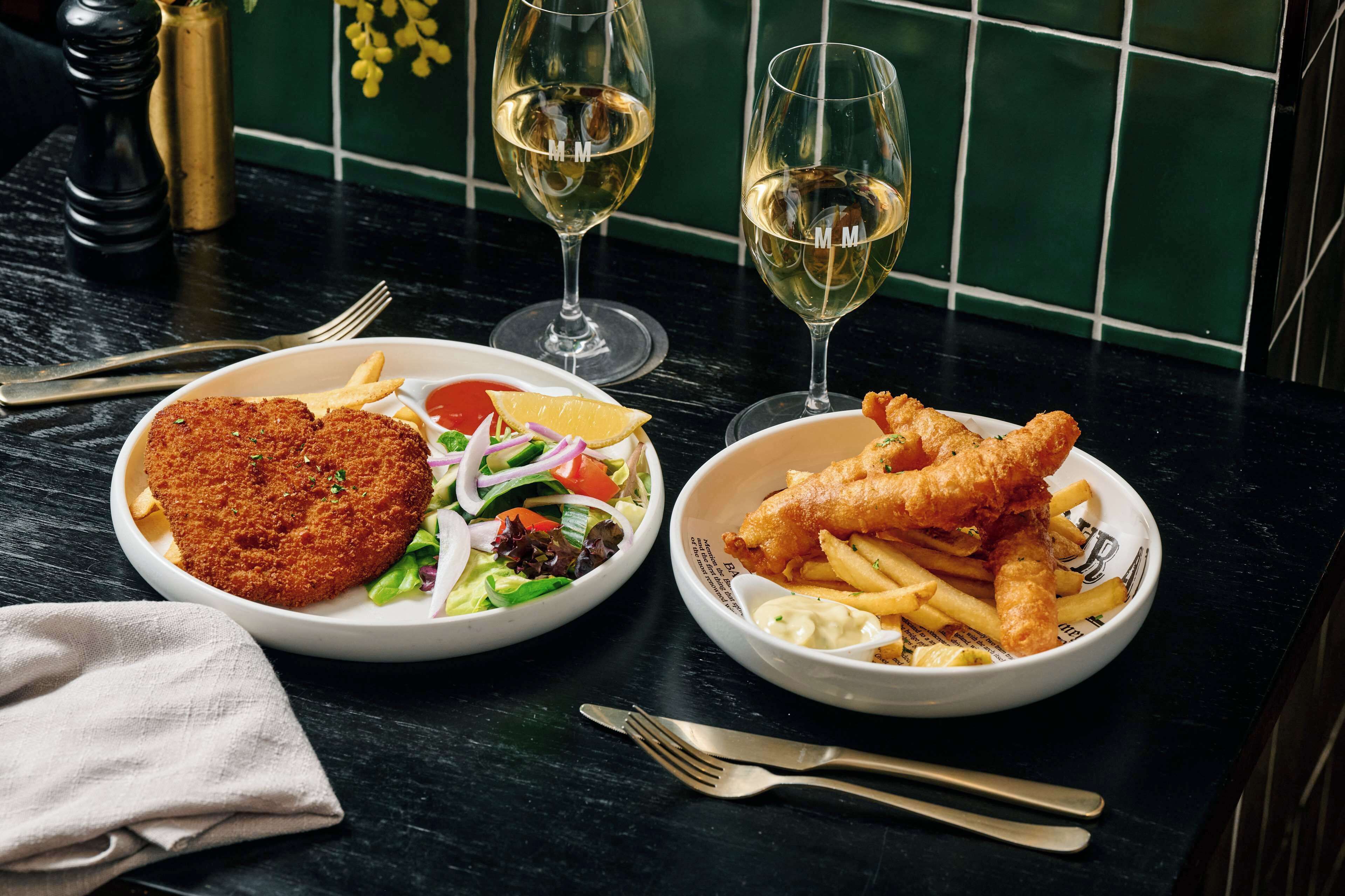 A table with two plates of food, a bottle of white wine, and a salt shaker.