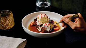 A bowl of dessert with ice cream and strawberries, a glass of water, and a textured glass on a table.