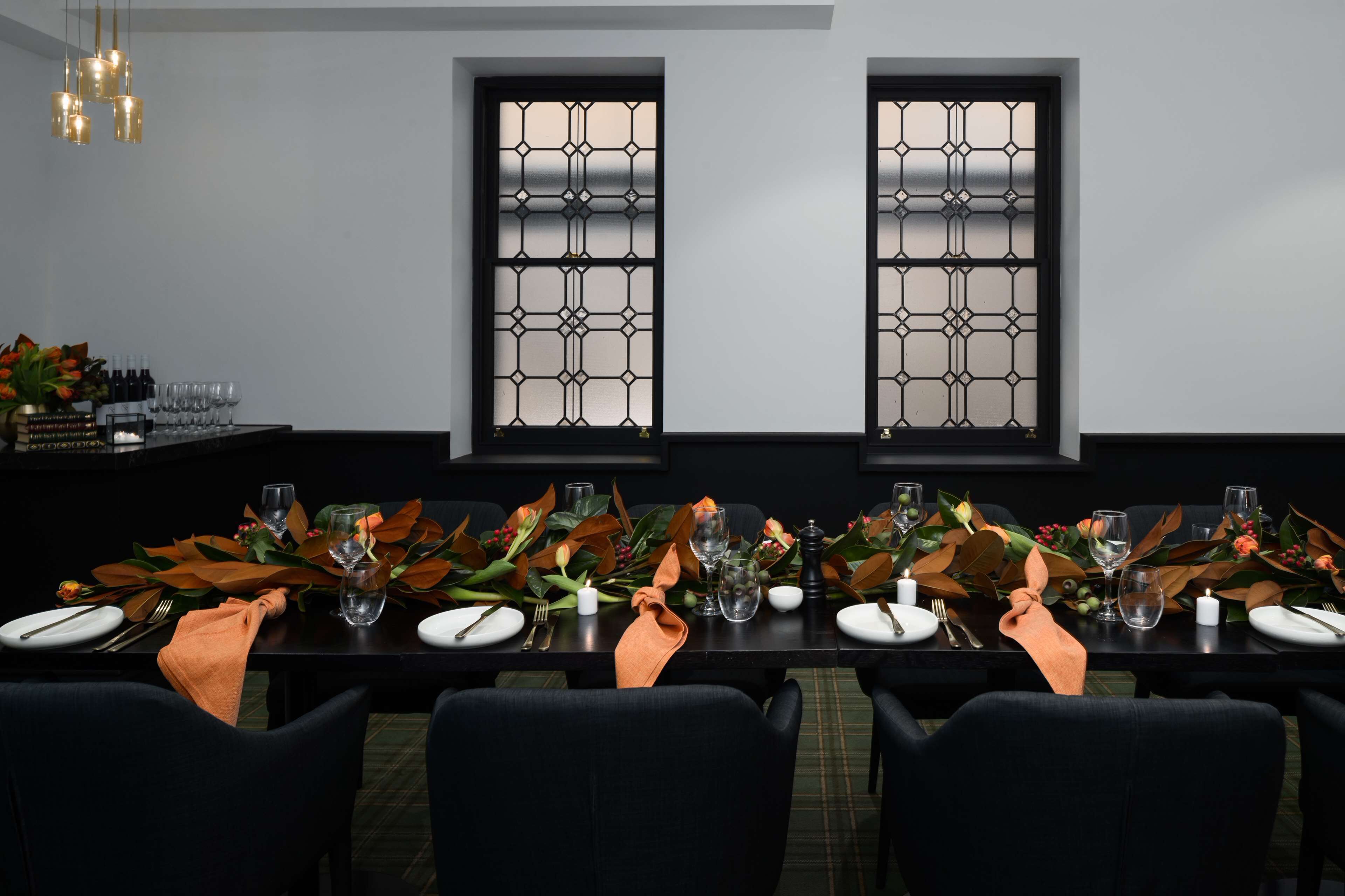 A dining table set for two with a dark wood finish, two windows with decorative grilles, and a chandelier with multiple light fixtures.
