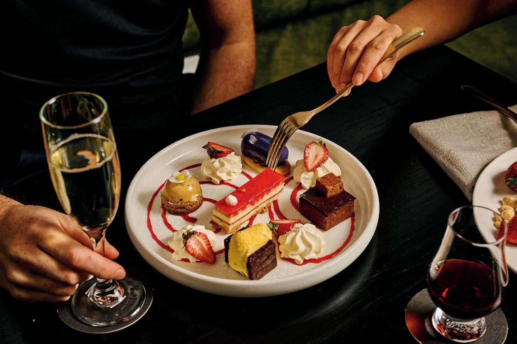A dessert plate with various sweets and a glass of white wine.