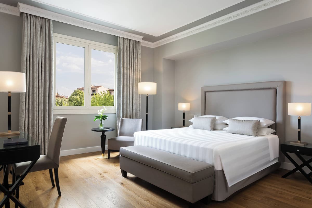 A modern hotel room with a large bed, a desk, a chair, and a small table.