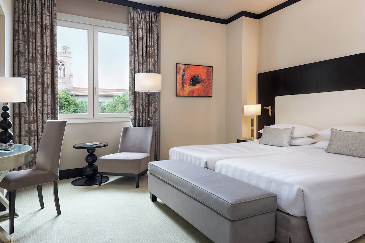 A hotel room with a large bed, a chair, a small table, and a window with curtains.