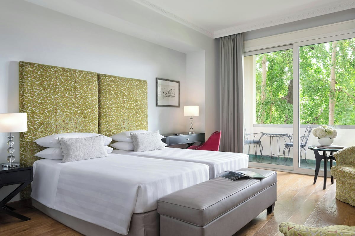 A hotel room with two beds, a desk, a chair, and a view of the outdoors.