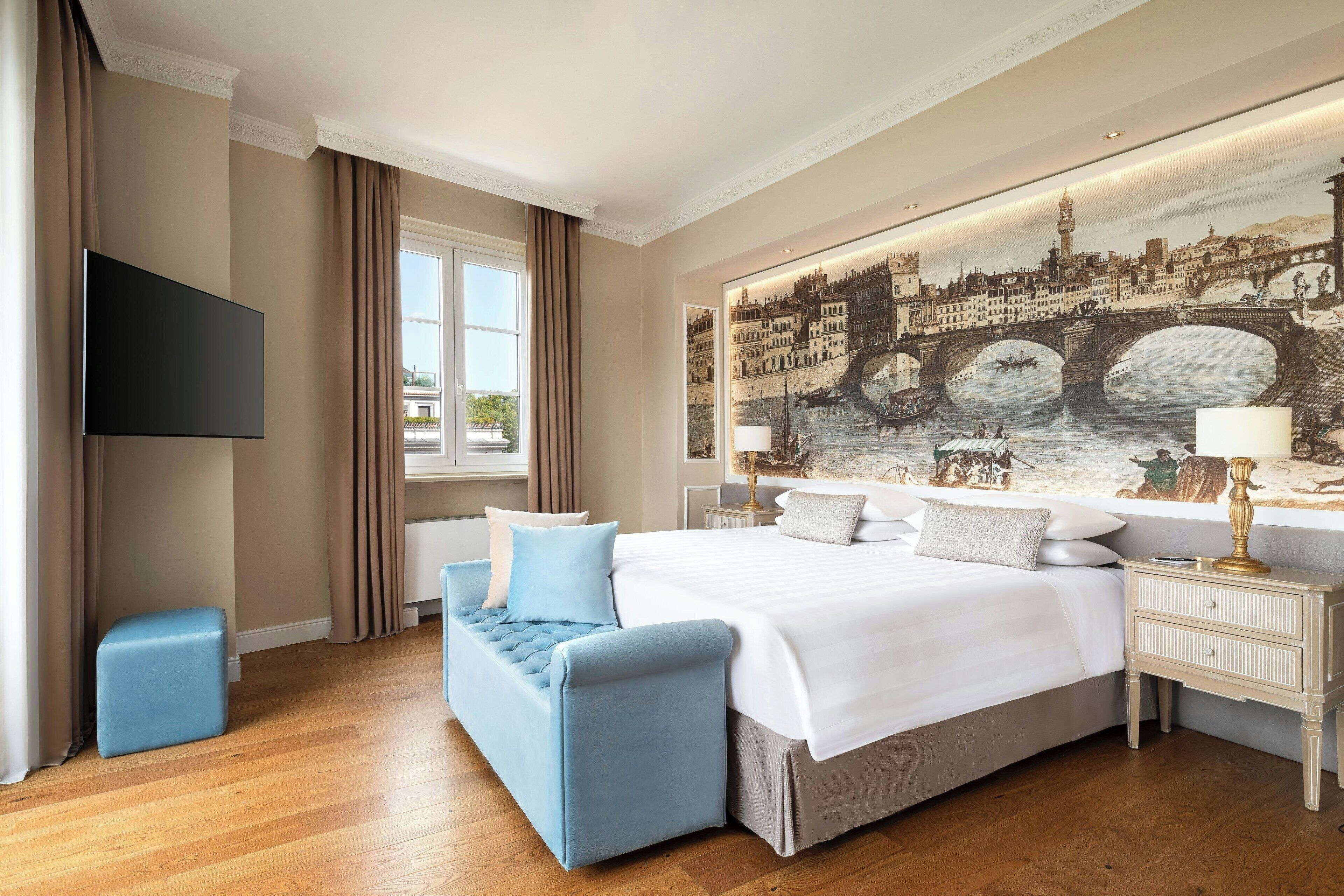 Une chambre d’hôtel avec un grand lit, un canapé bleu, un téléviseur à écran plat et une grande fresque murale représentant un paysage urbain.
