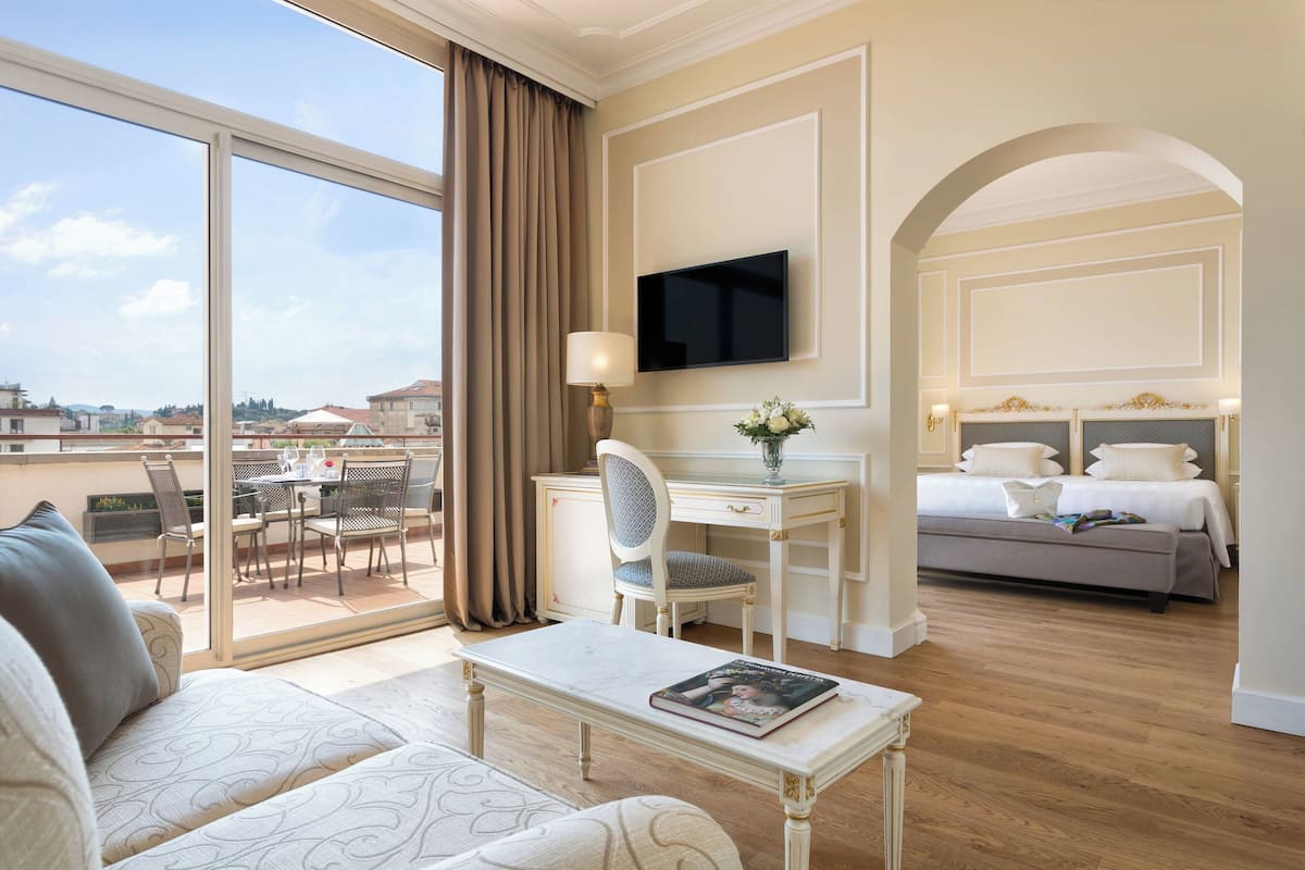 A hotel room with a balcony, a dining area, a TV, a bed, and a sofa.