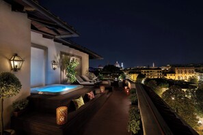 A rooftop terrace with a hot tub, lounge chairs, and ambient lighting.