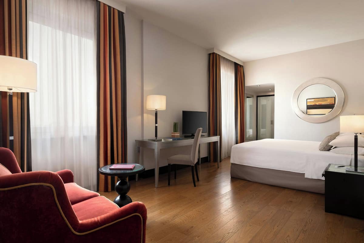 A hotel room with a bed, a desk with a chair, a TV, and a lamp.